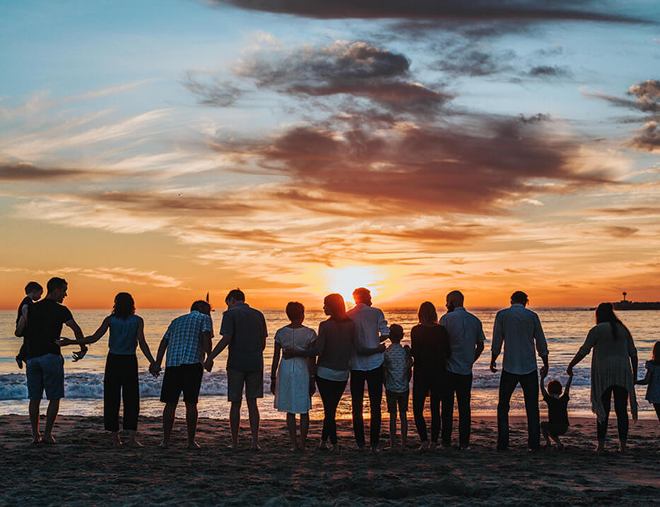 photo of a large family facing the ocean on a beach watching the sunset