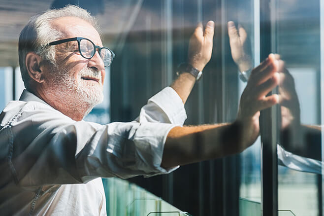 an older business man looks out high rise glass windows