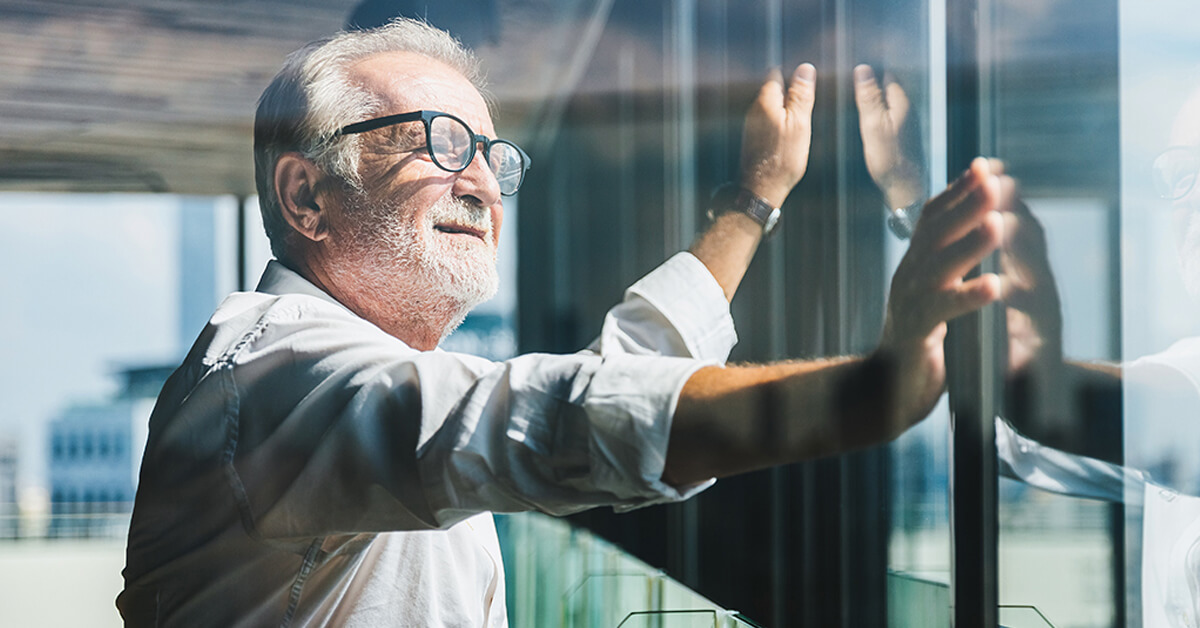 an older business man looks out high rise glass windows