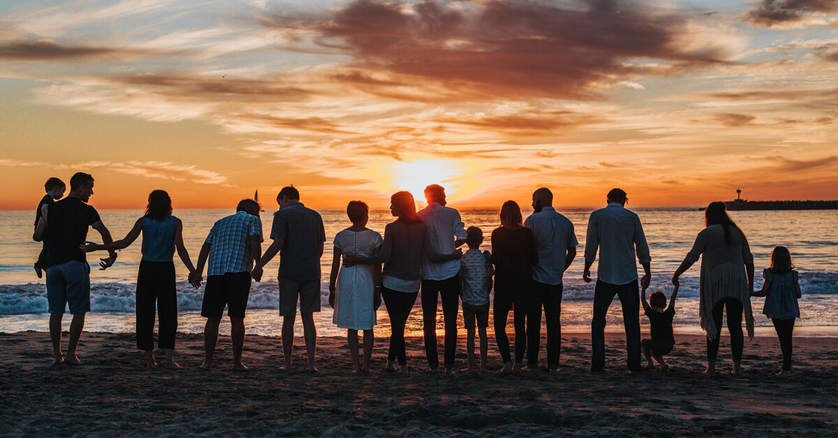 a larger family stands on the beach looking at the sunset