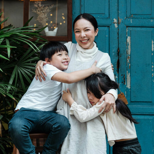 an Asian woman business owner smiles and stands outside her business with her two children