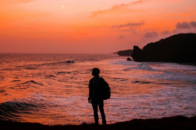 a person looks out onto the ocean at sunset