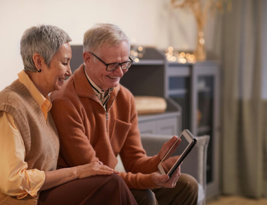 retired couple sits on a couch and views their tablet