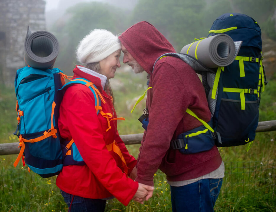 A retired couple faces each other and holds hands while hiking