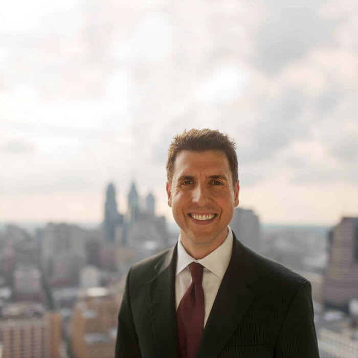 A photo of Steve De Cesare in a suit and tie against a city skyline