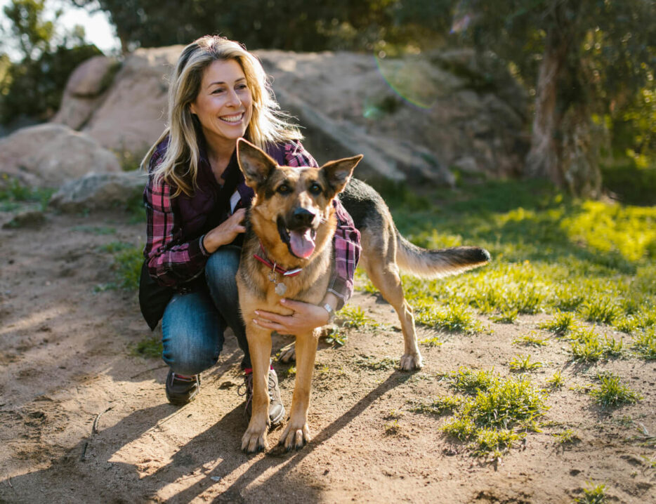 A blond woman hugs are German Shepard on a trail